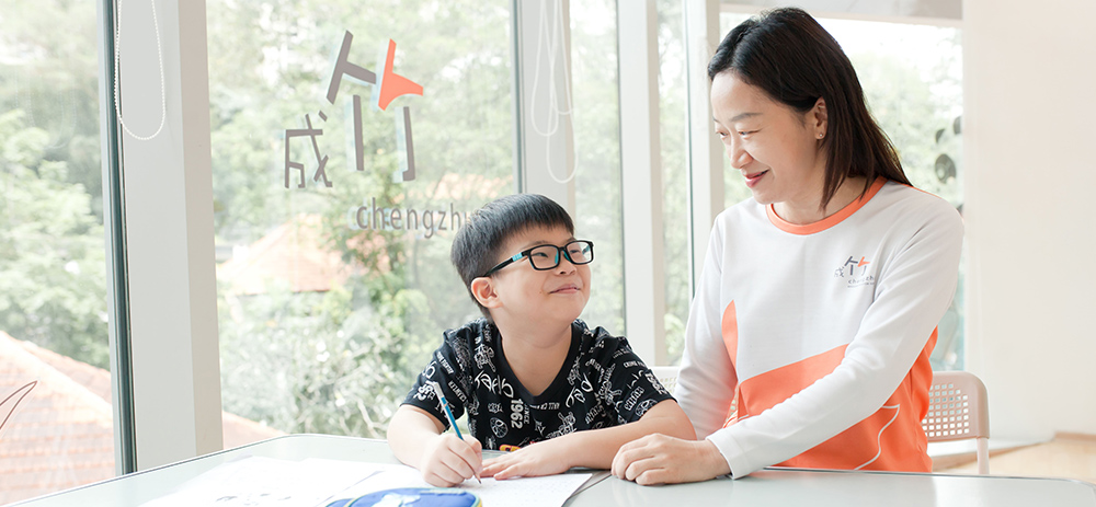 A-teacher-and-a-young-boy-engaged-in-writing-at-a-table-illustrating-a-learning-moment-in-Mandarin-classes-in-Singapore---Chengzhu-Mandarin-Centre