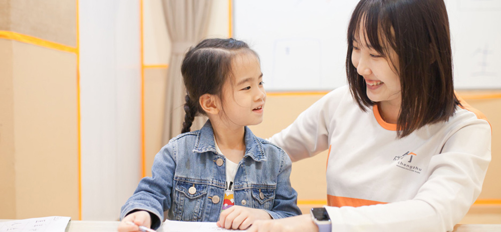 A-teacher-and-a-young-girl-sit-at-a-table-focused-on-a-notebook-sharing-a-moment-of-creativity-and-learning---Chengzhu-Mandarin-Centre