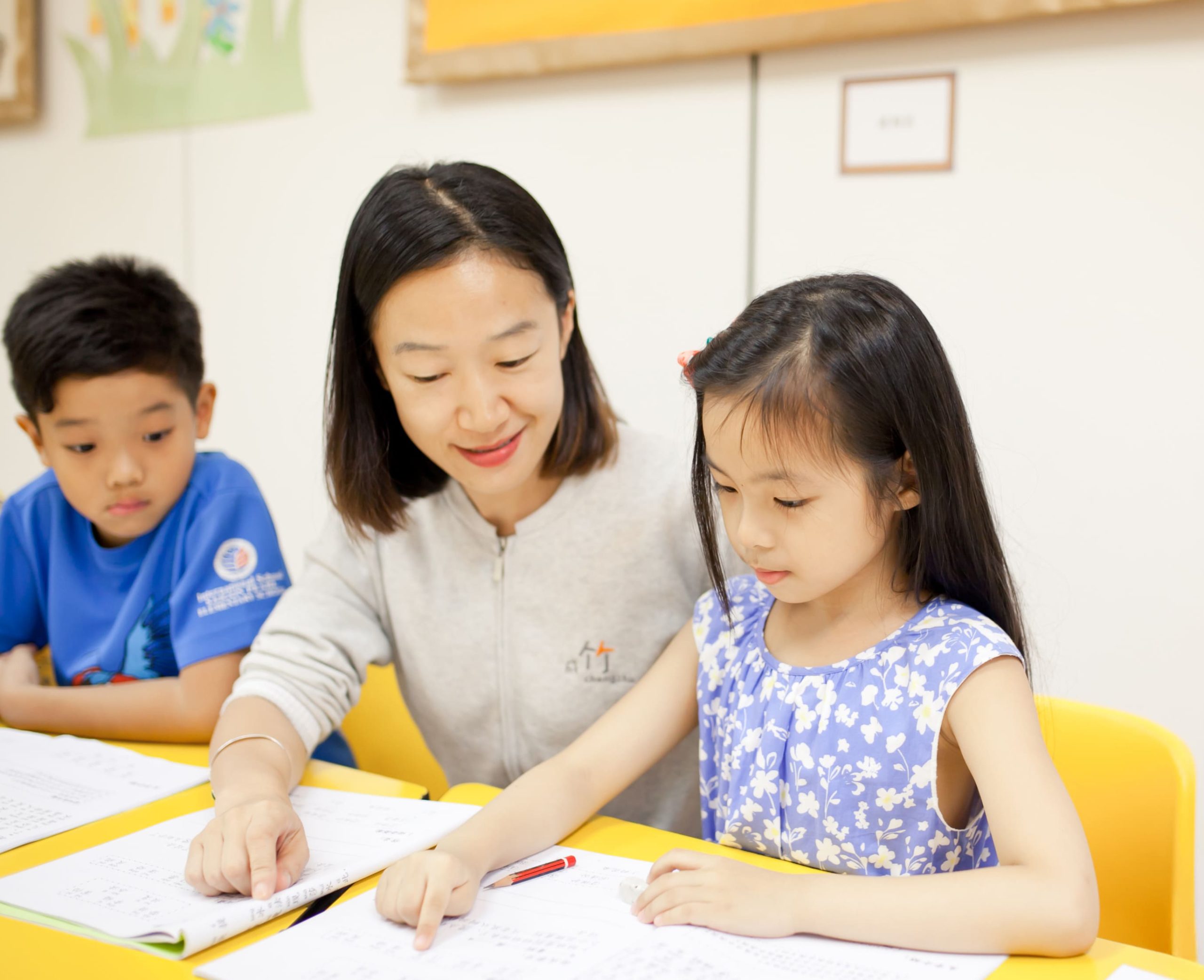 In-a-classroom-a-teacher-and-two-students-are-seated-at-a-table-concentrating-on-papers-as-they-learn-Mandarin-together---Chengzhu-Mandarin-Centre-crop